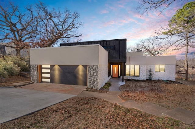 modern home featuring stone siding, an attached garage, driveway, and stucco siding