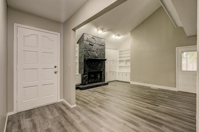 unfurnished living room with lofted ceiling, a fireplace, baseboards, and wood finished floors