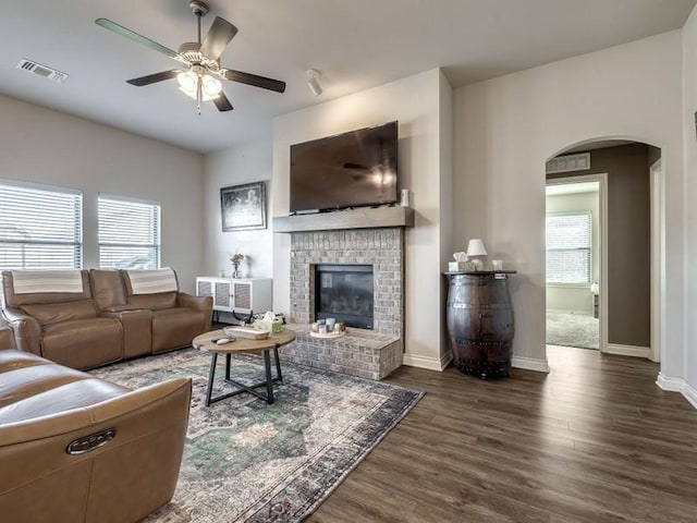 living area with arched walkways, visible vents, a brick fireplace, wood finished floors, and baseboards