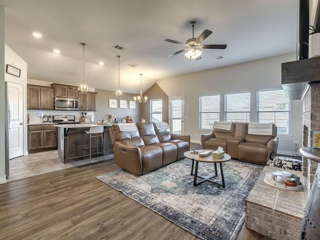 living area featuring lofted ceiling, light wood-style floors, visible vents, and ceiling fan with notable chandelier