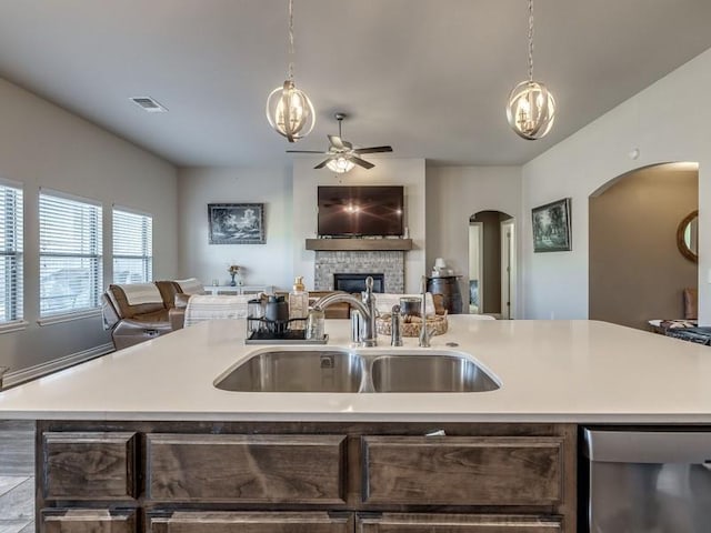 kitchen with a stone fireplace, a sink, open floor plan, light countertops, and stainless steel dishwasher