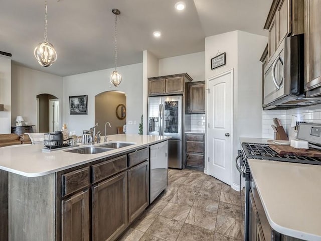 kitchen featuring arched walkways, tasteful backsplash, appliances with stainless steel finishes, a sink, and an island with sink