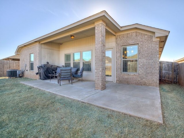 rear view of house with brick siding, a patio, a lawn, central AC, and a fenced backyard