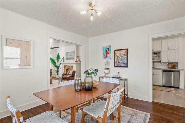 dining space featuring a textured ceiling, a fireplace, wood finished floors, and baseboards