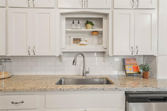 kitchen with stainless steel dishwasher, decorative backsplash, a sink, and white cabinets