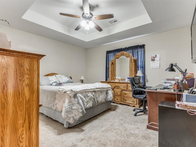 bedroom with carpet, visible vents, a tray ceiling, and ceiling fan