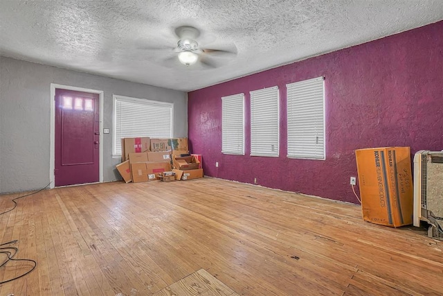 interior space with a textured ceiling, a textured wall, ceiling fan, and hardwood / wood-style flooring