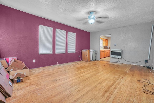 unfurnished living room featuring heating unit, light wood finished floors, ceiling fan, and a textured wall