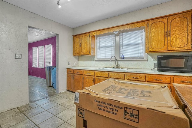 kitchen with brown cabinets, black microwave, light countertops, and a sink