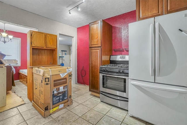 kitchen with freestanding refrigerator, stainless steel gas range, a textured ceiling, a chandelier, and light tile patterned flooring