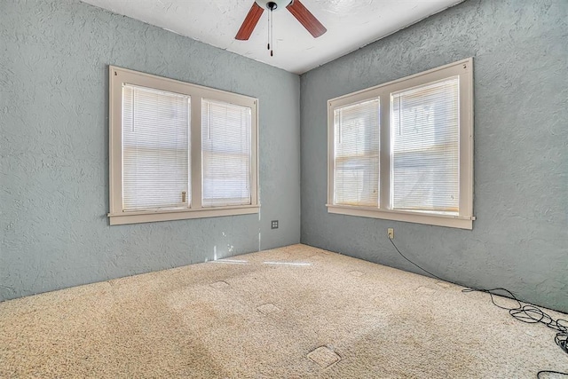 carpeted spare room with ceiling fan, a wealth of natural light, and a textured wall