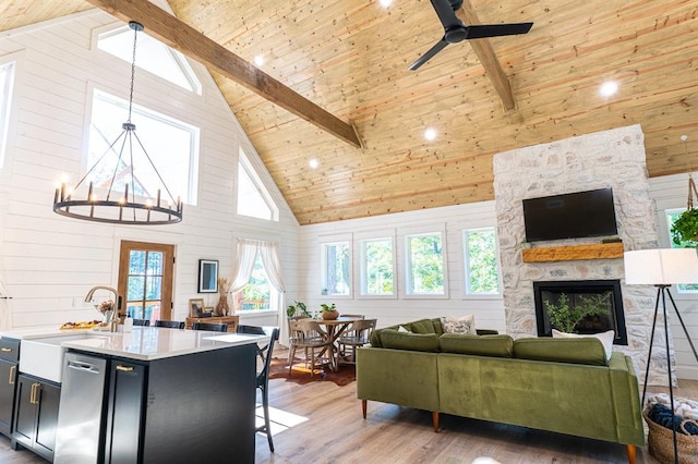 living room with wood ceiling, light wood-style floors, a fireplace, beam ceiling, and ceiling fan with notable chandelier