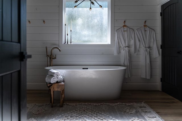 full bath featuring a freestanding bath, wood finished floors, and wooden walls