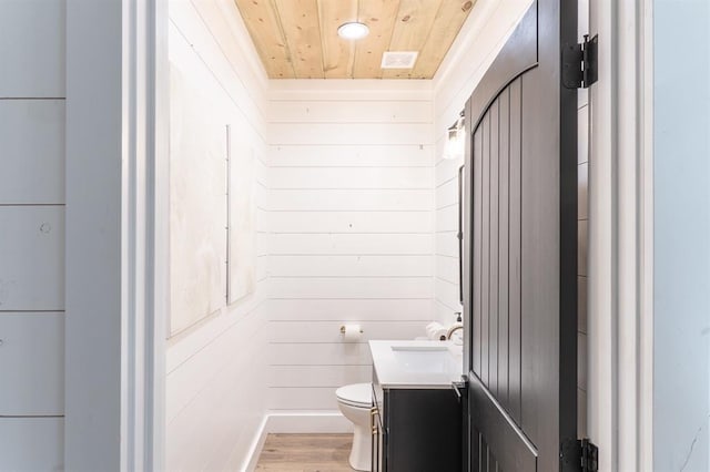 half bathroom with toilet, wood walls, vanity, wood finished floors, and wooden ceiling