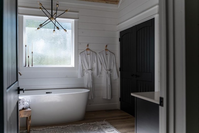 full bathroom featuring a healthy amount of sunlight, wooden walls, a freestanding bath, and wood finished floors