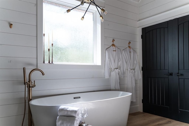 bathroom with wooden walls, a freestanding bath, and wood finished floors