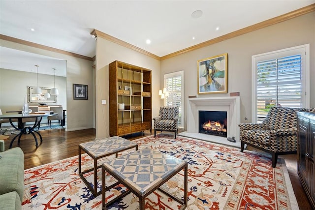 living room with baseboards, ornamental molding, a warm lit fireplace, and wood finished floors