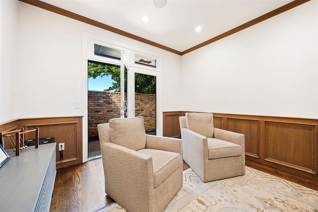 sitting room with wainscoting, recessed lighting, ornamental molding, and light wood finished floors