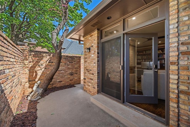 doorway to property featuring brick siding, fence, and a patio area