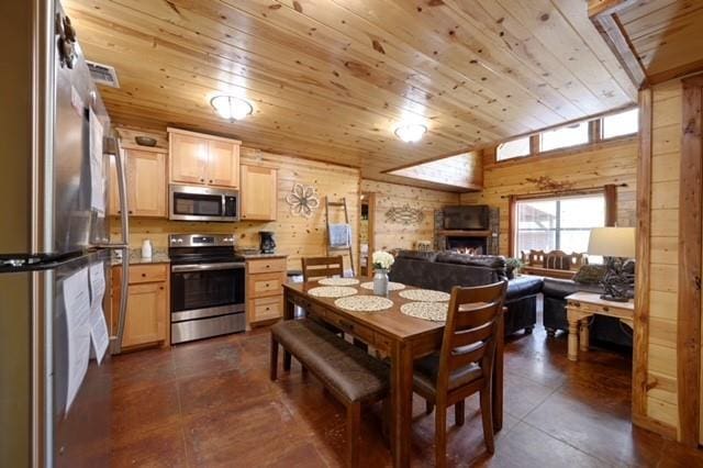 kitchen featuring light brown cabinets, wooden walls, stainless steel appliances, wood ceiling, and a lit fireplace