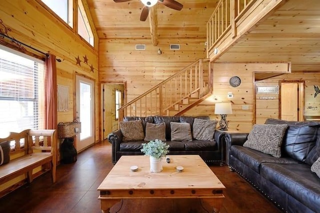 living room with visible vents, stairway, wood walls, ceiling fan, and high vaulted ceiling