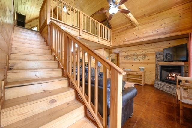 stairway featuring wooden walls, a ceiling fan, wood ceiling, a stone fireplace, and high vaulted ceiling