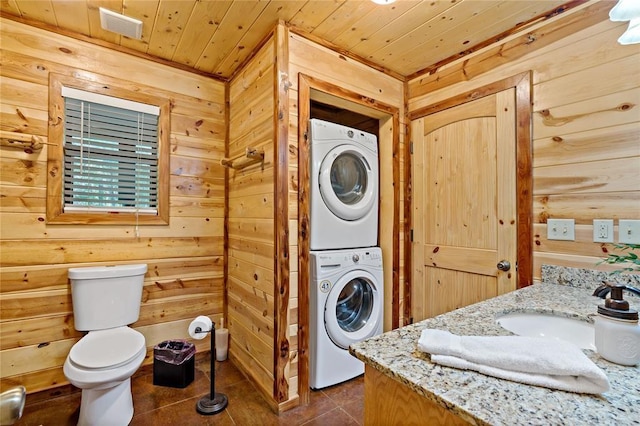 clothes washing area with wood ceiling, a sink, wood walls, stacked washing maching and dryer, and dark tile patterned floors