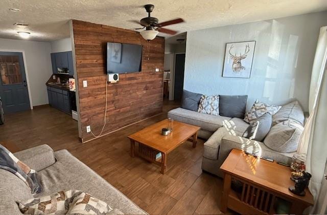 living room featuring dark wood-style floors, wooden walls, a textured ceiling, and a ceiling fan