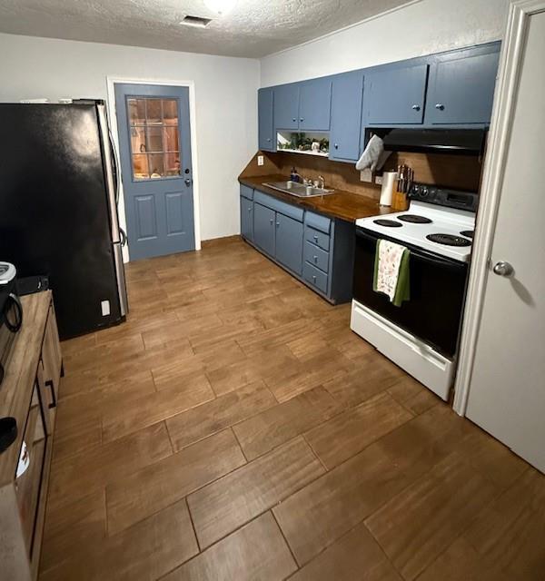 kitchen featuring blue cabinets, light wood-type flooring, visible vents, white electric range, and freestanding refrigerator