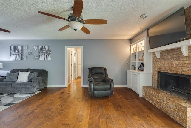 living room with a textured ceiling, a ceiling fan, a brick fireplace, and hardwood / wood-style flooring