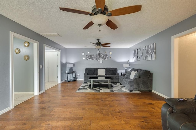 living area with ceiling fan, a textured ceiling, baseboards, and wood-type flooring