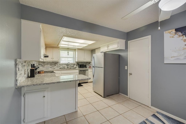 kitchen featuring a peninsula, tasteful backsplash, a textured ceiling, light tile patterned floors, and appliances with stainless steel finishes