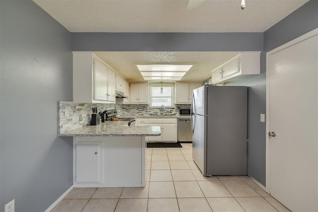 kitchen featuring a peninsula, a sink, under cabinet range hood, appliances with stainless steel finishes, and tasteful backsplash