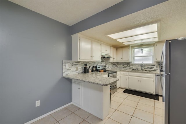 kitchen with stainless steel appliances, a sink, a peninsula, light tile patterned floors, and decorative backsplash