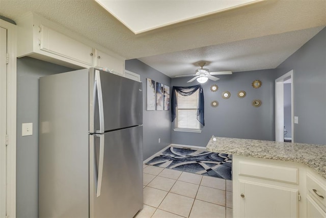 kitchen featuring light tile patterned floors, a ceiling fan, freestanding refrigerator, a textured ceiling, and baseboards