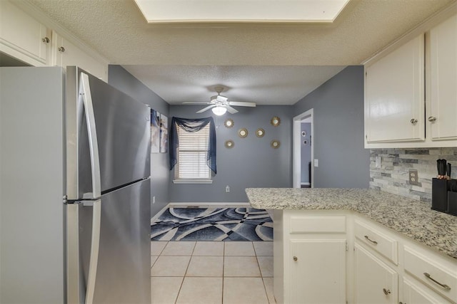 kitchen featuring light tile patterned floors, a ceiling fan, freestanding refrigerator, a textured ceiling, and backsplash