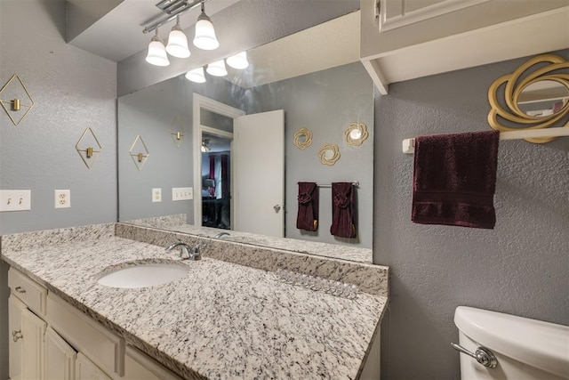 bathroom featuring toilet, vanity, and a textured wall
