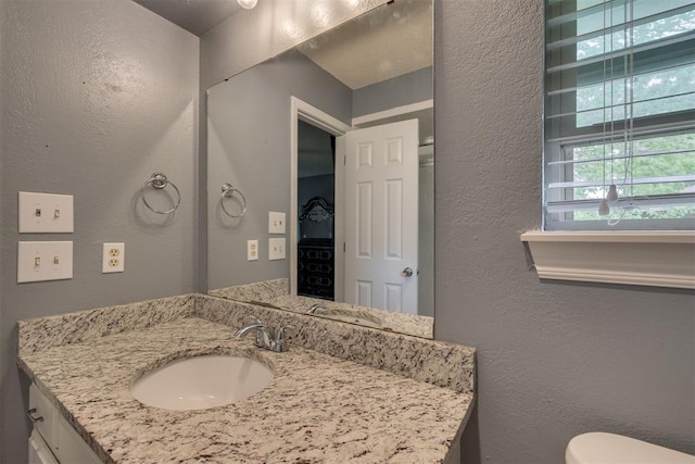 half bathroom with toilet, vanity, and a textured wall