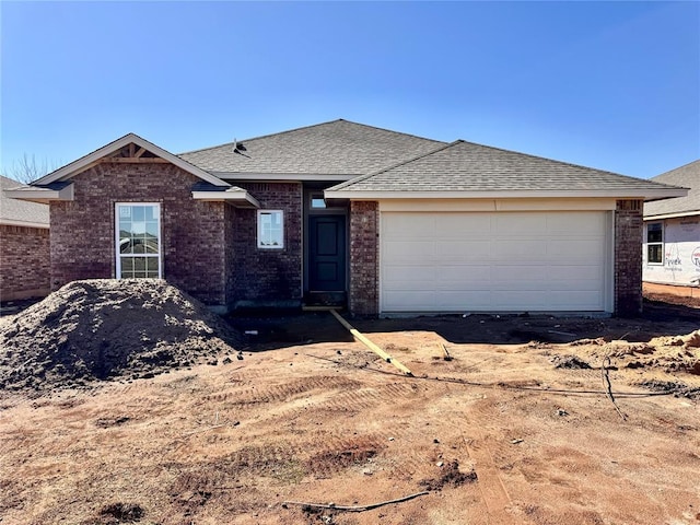 single story home with a garage, brick siding, and a shingled roof