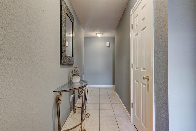 hallway with light tile patterned floors, baseboards, and a textured wall