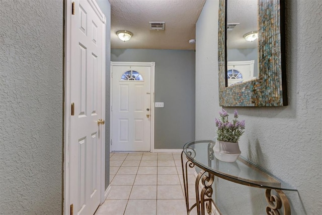 entryway featuring a textured ceiling, a textured wall, light tile patterned flooring, and visible vents