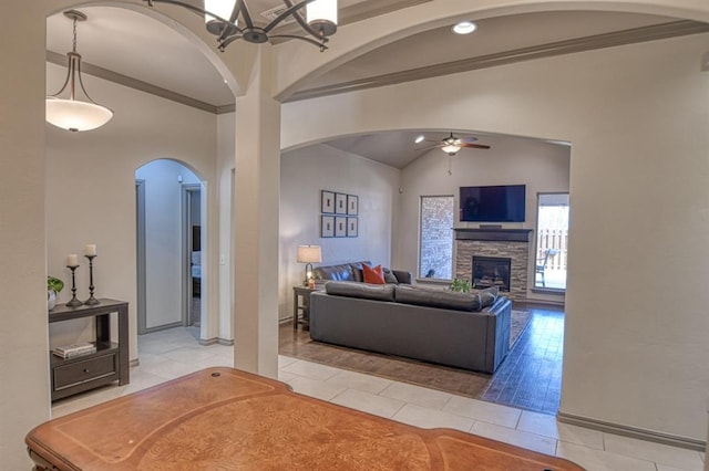 living area with a stone fireplace, light tile patterned flooring, a ceiling fan, vaulted ceiling, and ornamental molding