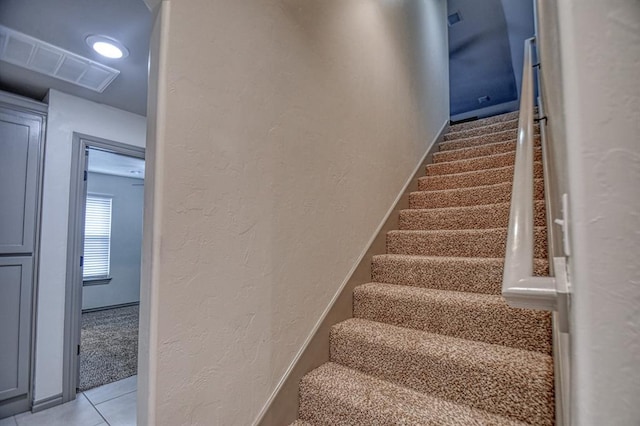 staircase featuring visible vents, a textured wall, baseboards, and tile patterned floors