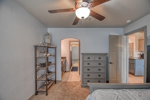 bedroom featuring light tile patterned floors, visible vents, arched walkways, a ceiling fan, and light colored carpet