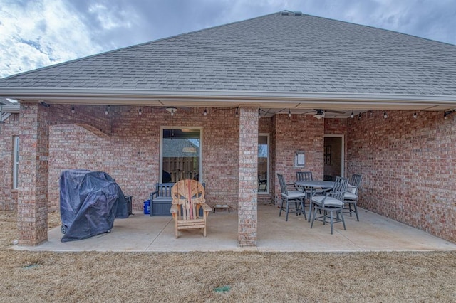 back of house featuring brick siding, a ceiling fan, roof with shingles, outdoor dining space, and a patio area