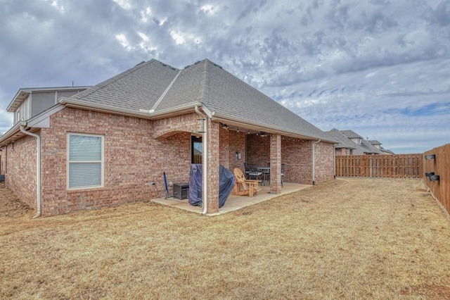 rear view of property featuring brick siding, a shingled roof, a lawn, a patio area, and a fenced backyard