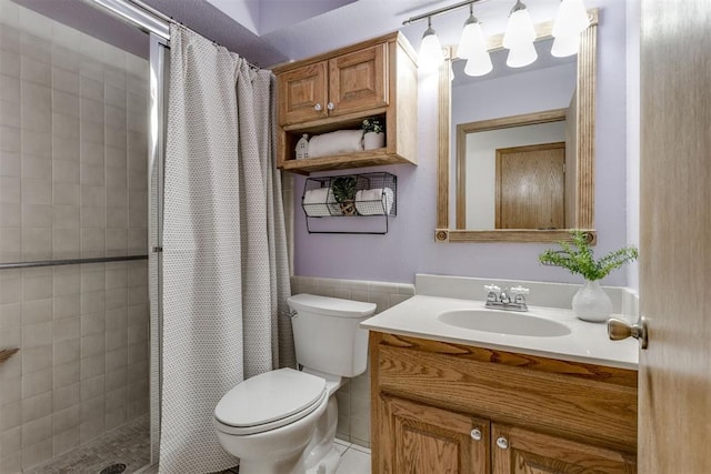 bathroom with toilet, vanity, tile walls, wainscoting, and a tile shower