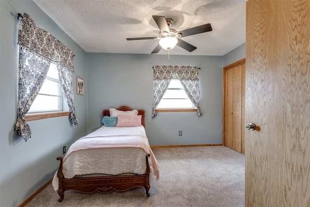 carpeted bedroom with a textured ceiling, multiple windows, a ceiling fan, and baseboards