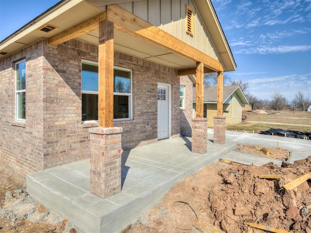 doorway to property featuring a patio, brick siding, and board and batten siding