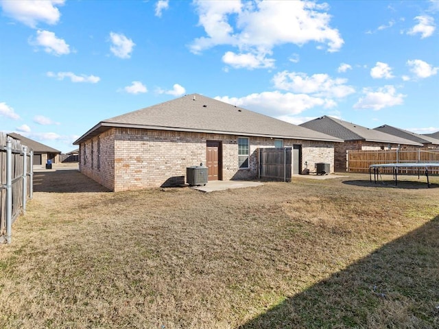 back of house featuring a trampoline, brick siding, a lawn, and a fenced backyard